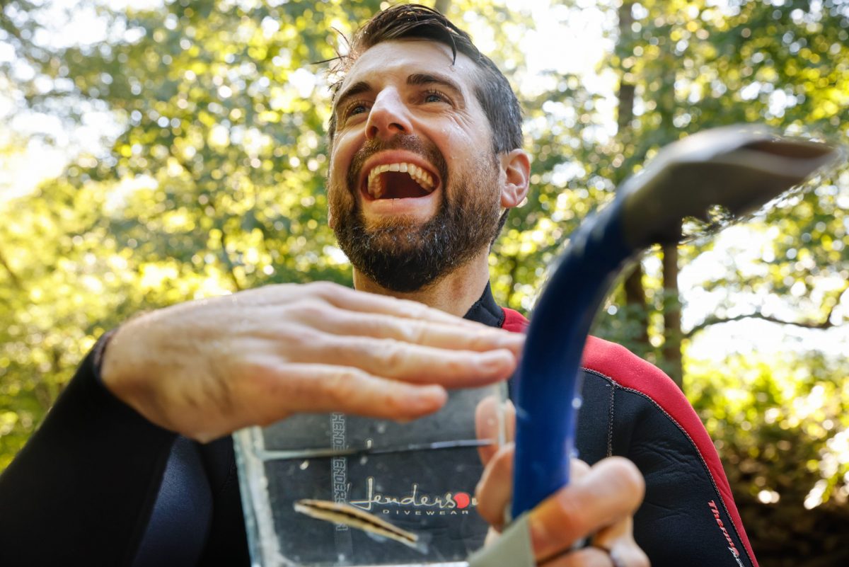 Man in a wetsuit laughs while holding container with freshwater fish in a stream