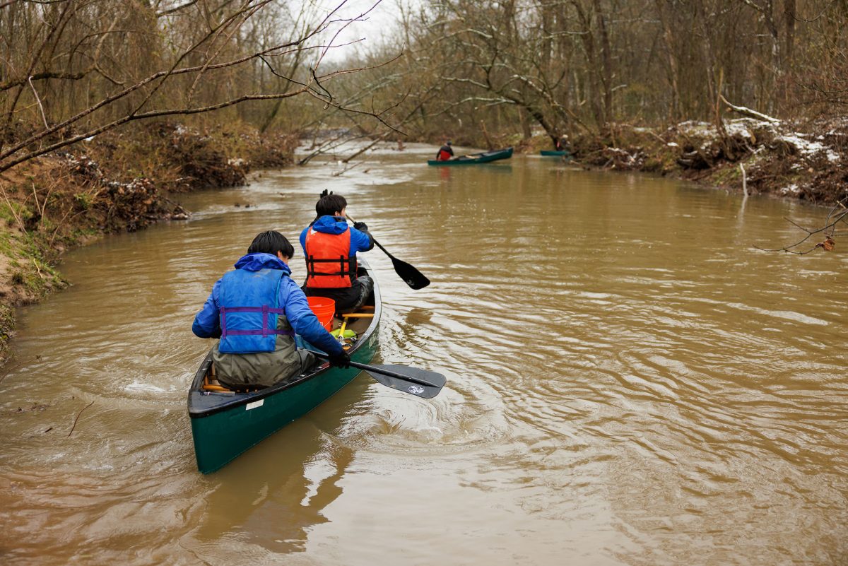 Two people paddle a canoe down a stream