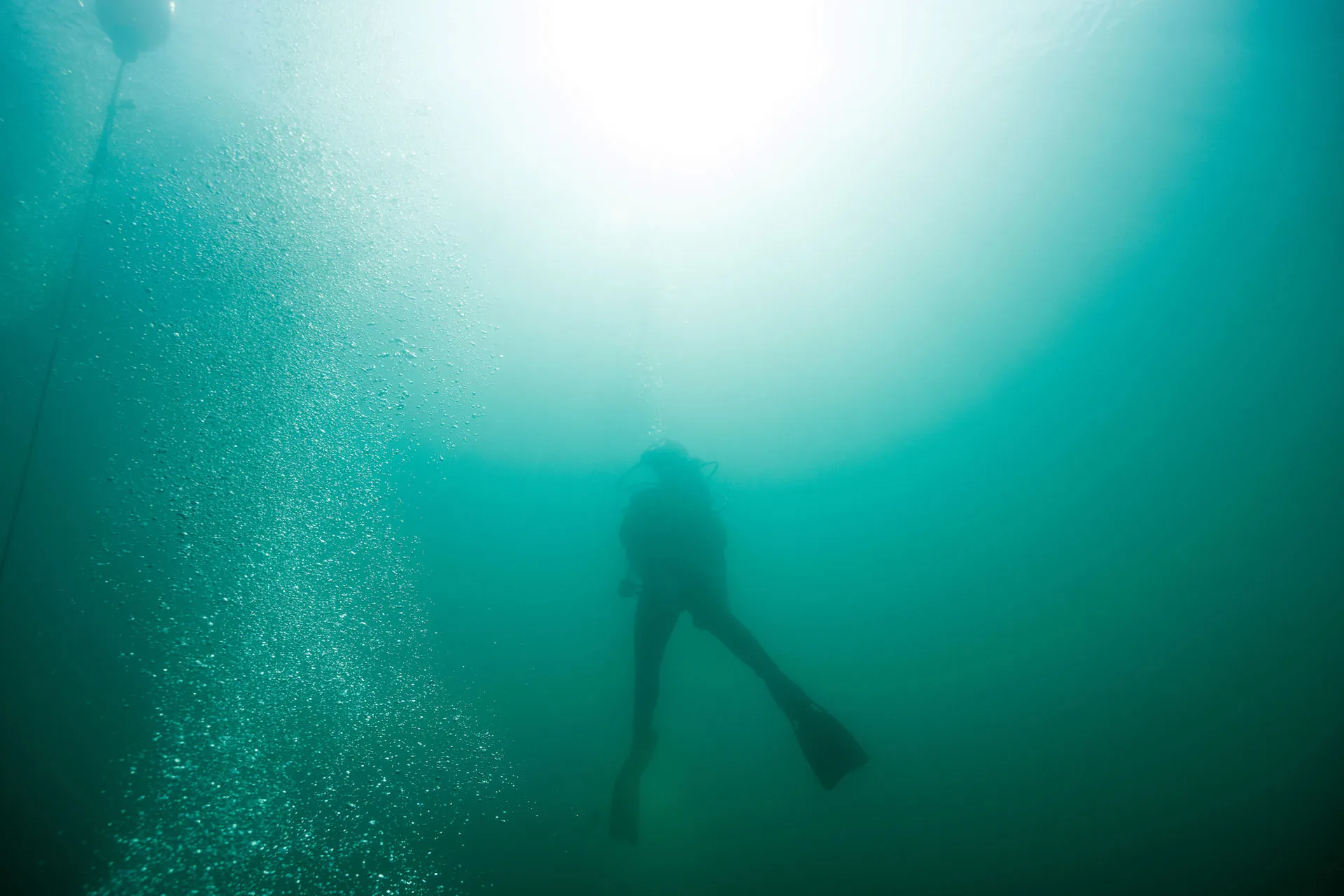 A SCUBA diver is silhouetted against sunlight as they swim towards the surface in a quarry