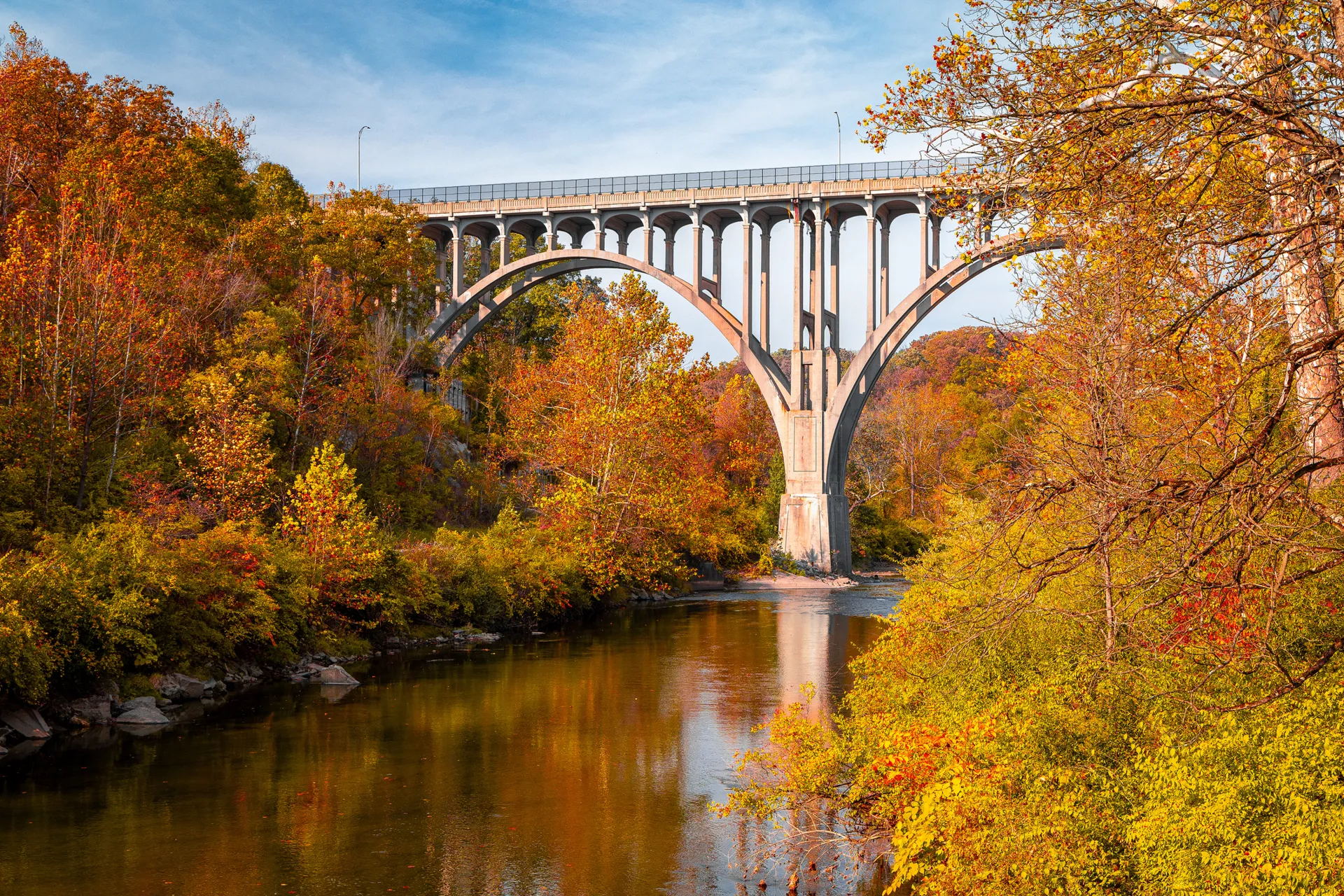 The Cuyahoga River flows through Cuyahoga Valley National Park. The image is taken durign the fall with colorful foliages, waterfalls, rail tracks and trains visible.