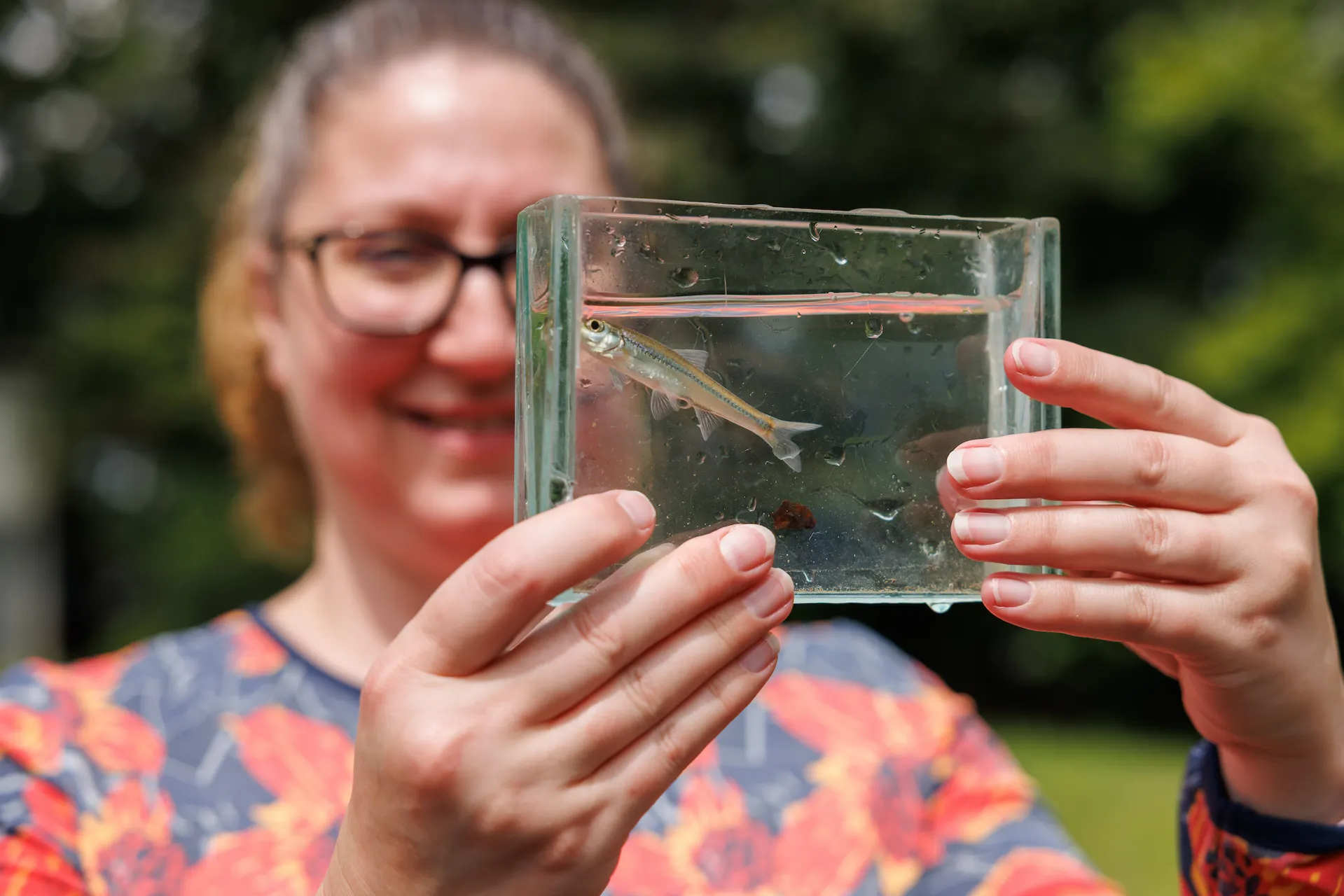 An educator holding up a viewing container of water and a freshwater fish during 