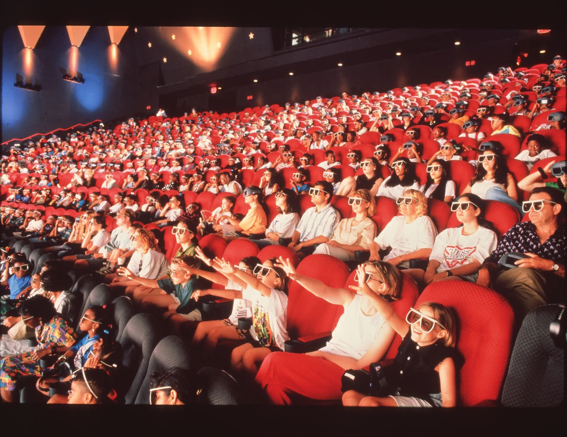 A theater full of people sitting in a red seats wearing 3D glasses